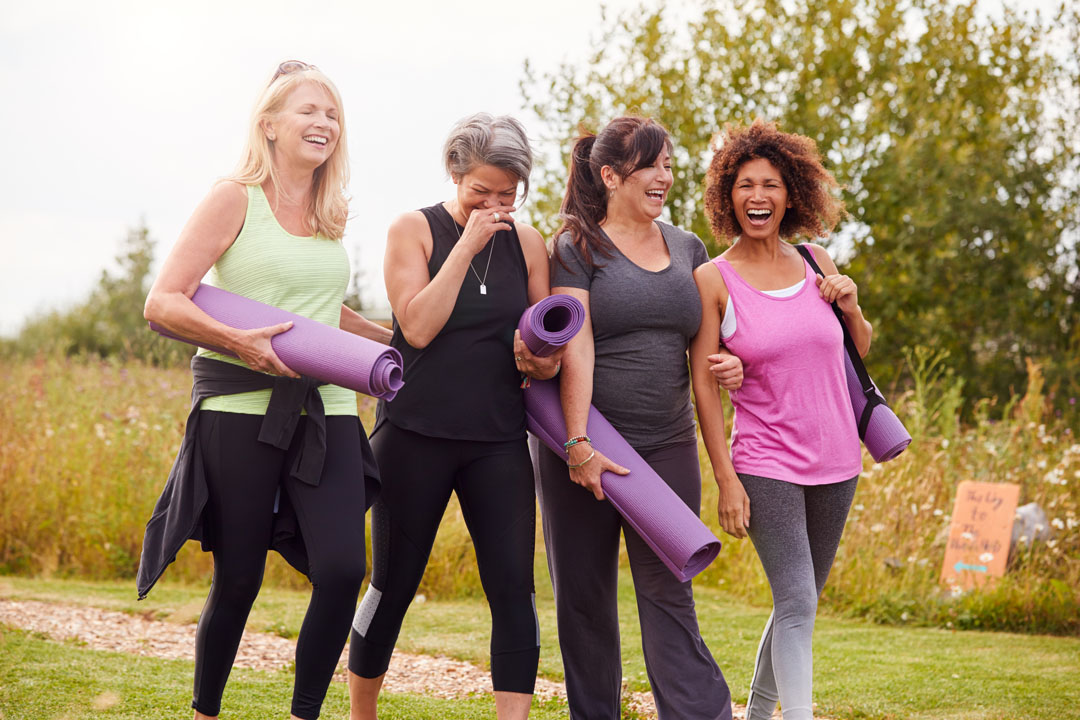 Group Of Mature Female Friends On Outdoor Yoga Retreat Walking Along Path Through Campsite